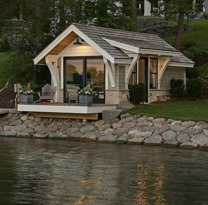 Small unique tiny home with porch and seating area by a rocky lakeside, showcasing clever off the grid living design.
