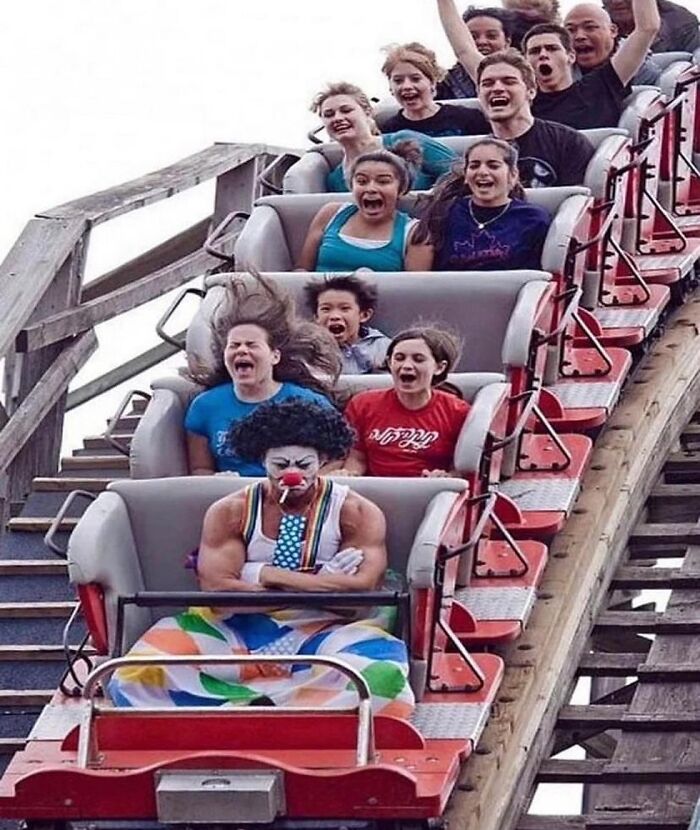 Clown sitting expressionless on a roller coaster, surrounded by screaming riders, illustrating a random cursed image.