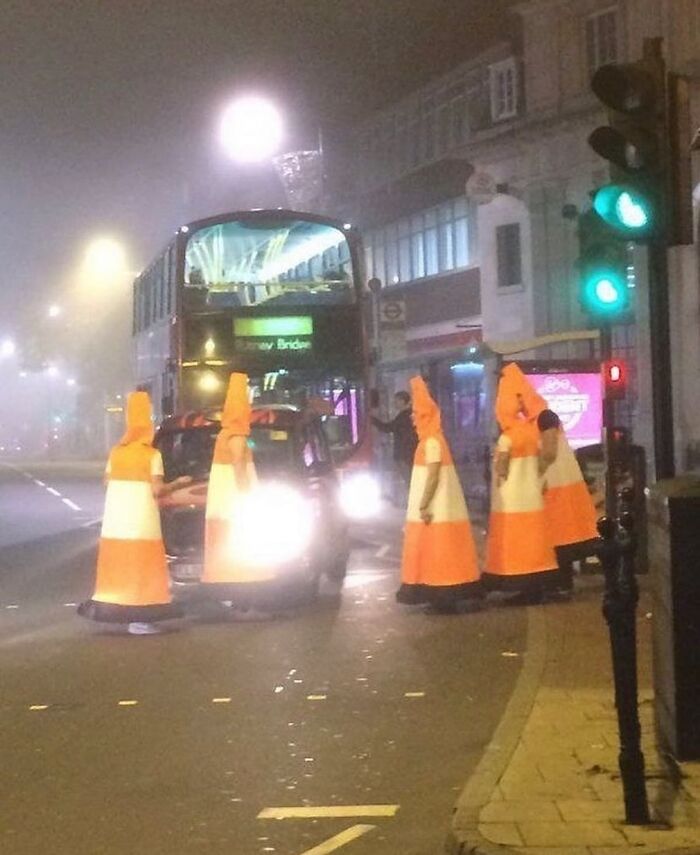 People dressed as traffic cones stand in front of a taxi at night, illustrating a random cursed image scenario.