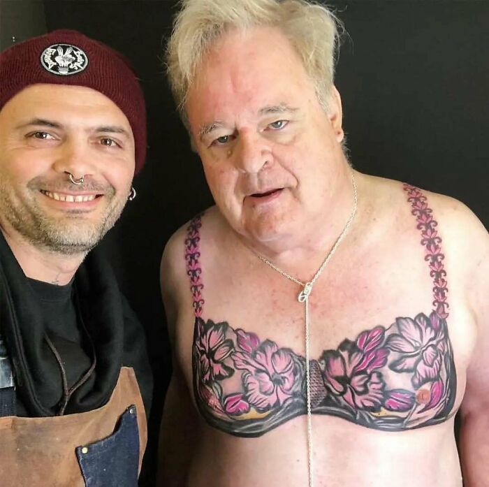 Man with hilariously bad tattoo of a floral bra, posing with an artist in a beanie.