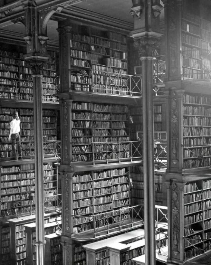 Vintage library interior with towering bookshelves and a person accessing books in a historic setting showing history up close.