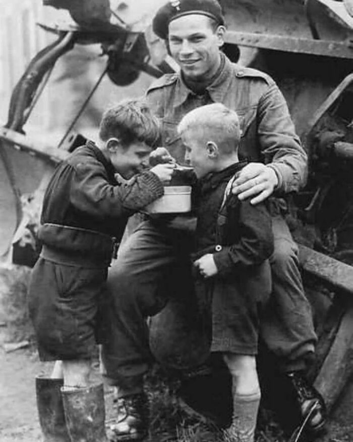 Soldier with two children sharing a meal near military equipment in a vintage photo showing history up close.