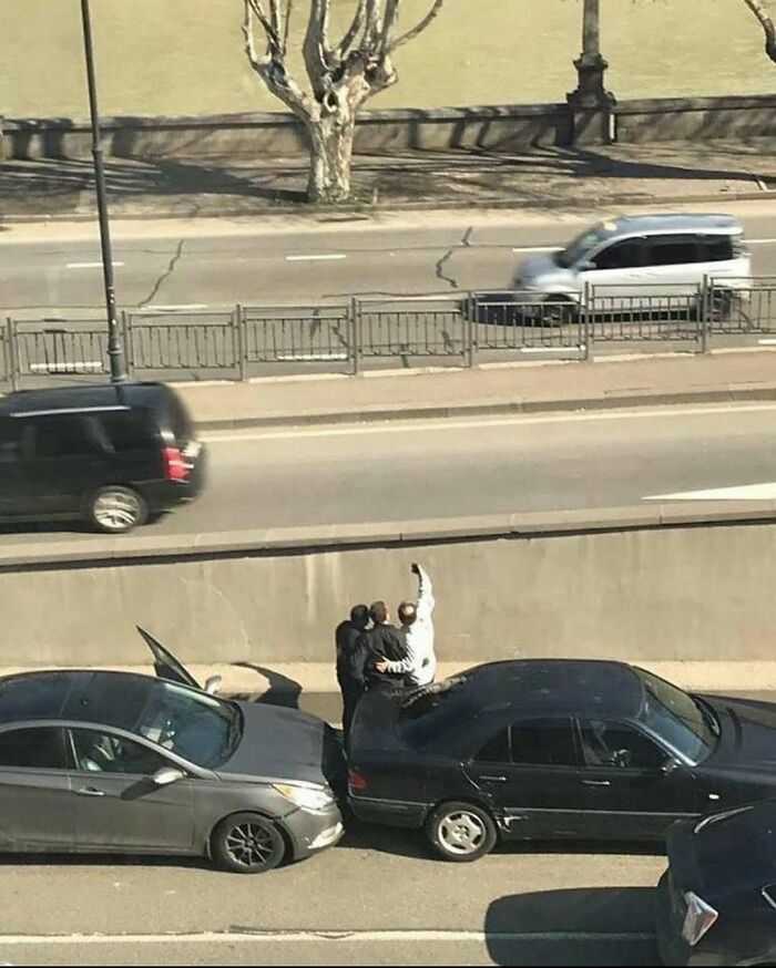 Three people taking a selfie on the highway between two parked cars, representing random cursed images.