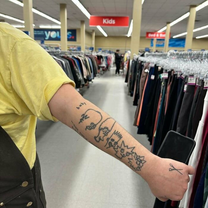Forearm with Simpsons tattoos in a clothing store aisle, featuring quirky designs.