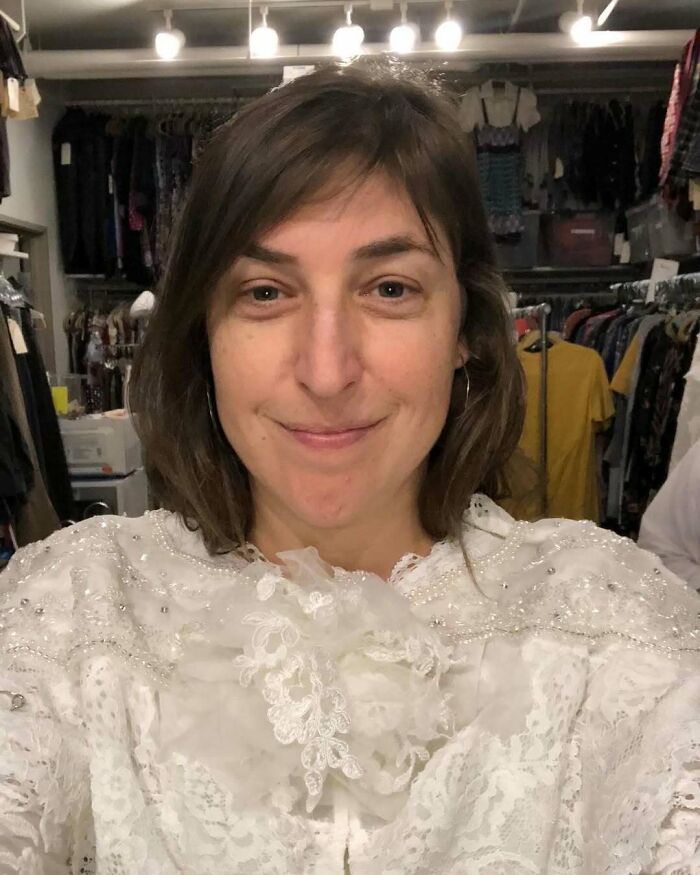 Woman smiling in a clothing store surrounded by vintage garments, reflecting celebrity encounters that went well or badly.