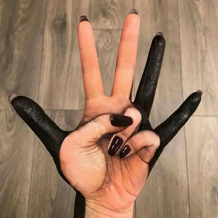 Black ink tattoo on a hand, creating an optical illusion of a smaller hand, showcasing hilariously bad tattoos.