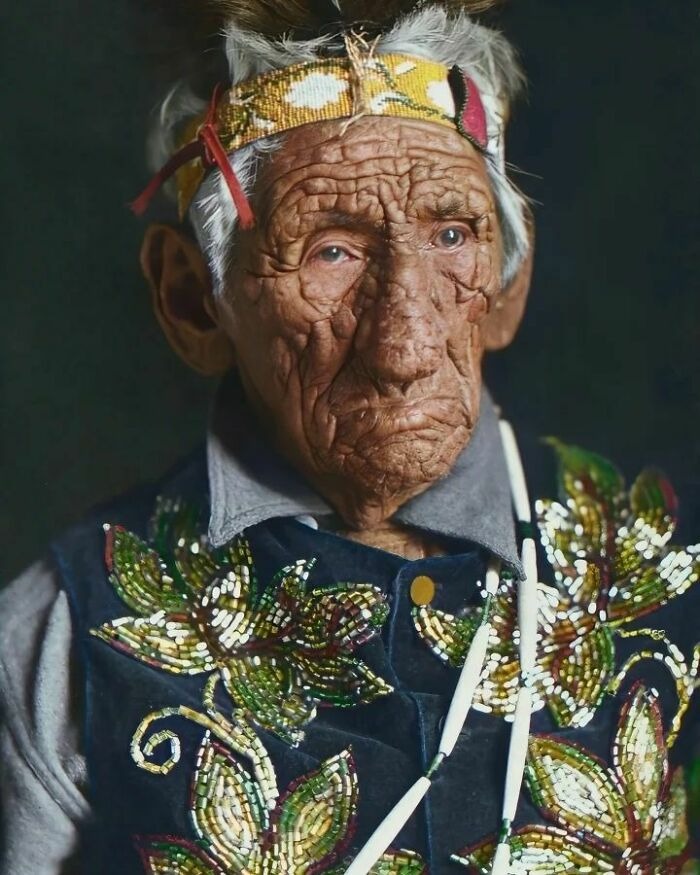 Elderly man in traditional beaded clothing and headband, showcasing vintage history through a close-up portrait.
