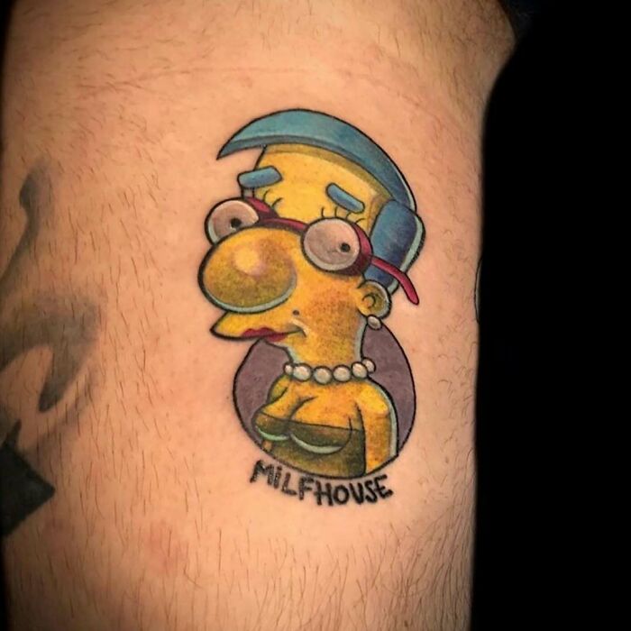 A humorous Simpsons tattoo featuring Milhouse with exaggerated features on a person's skin.