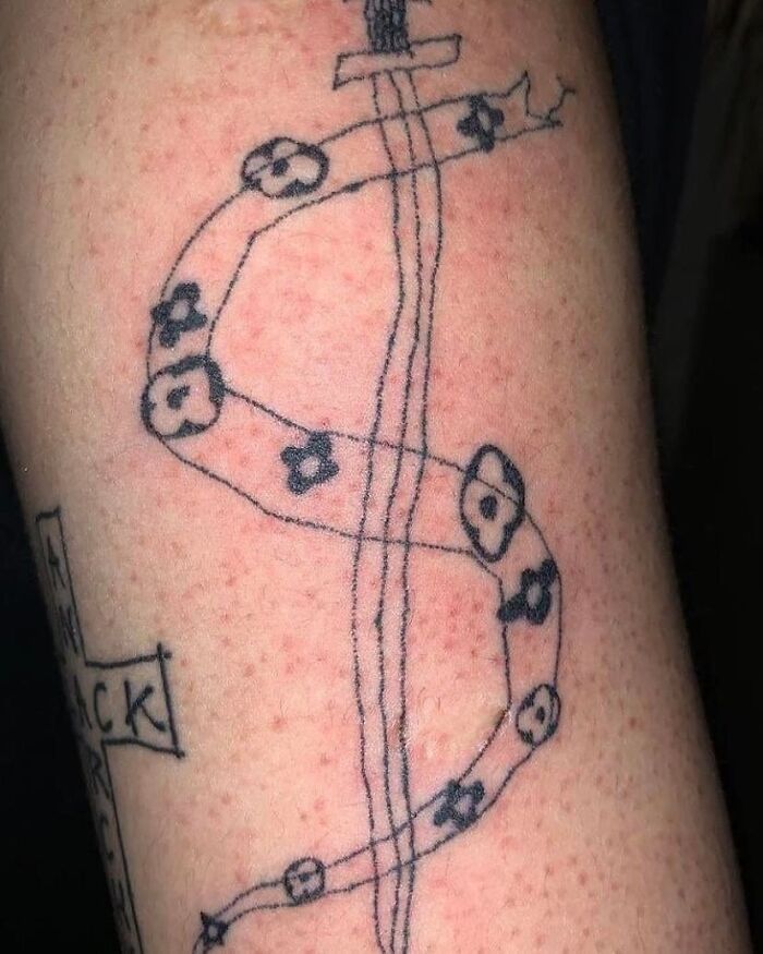 Unusual tattoo of a sword with ribbon and flowers on skin, highlighting permanent mistakes in ink.