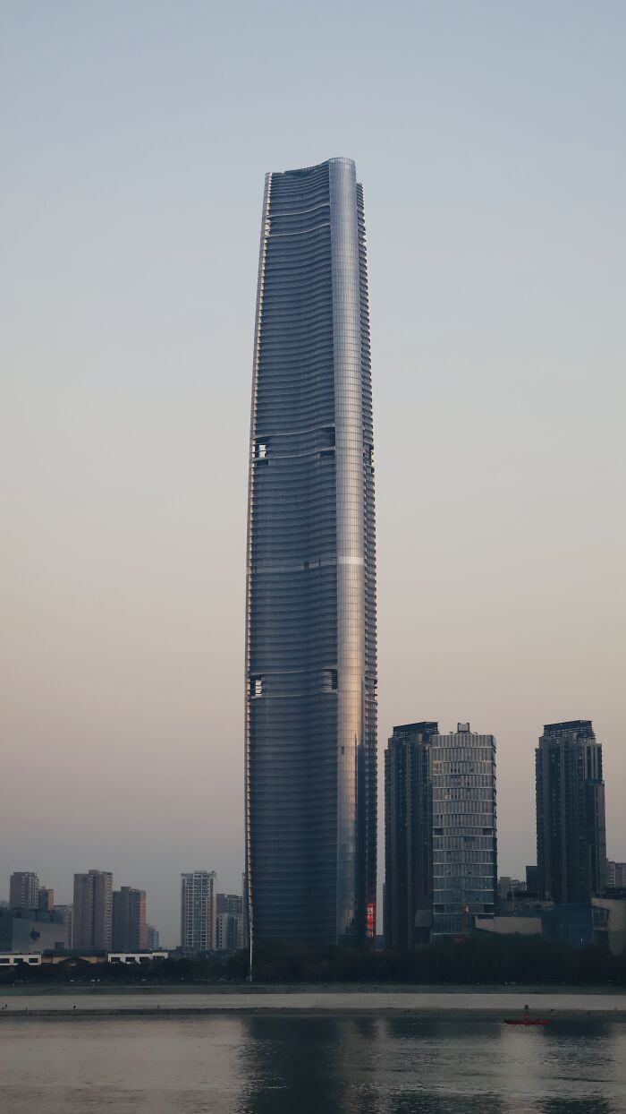 Skyscraper at sunset, part of the world's tallest buildings, with water in the foreground and smaller buildings nearby.