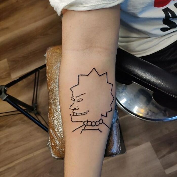Arm featuring a simple line tattoo of a Simpsons character.