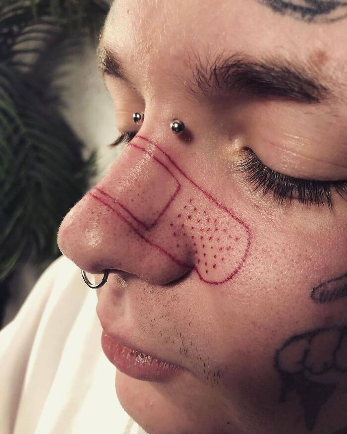 Close-up of a person's nose with a whimsical poorly-drawn band-aid tattoo, highlighting bad tattoo design.