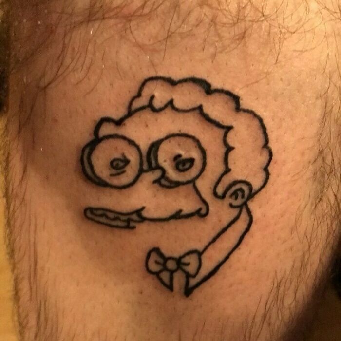 Cartoon character tattoo attempt with glasses and bowtie, resembling a rough sketch from The Simpsons series.