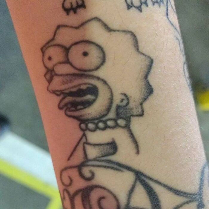 Tattoo of a distorted Simpsons character on forearm, highlighting unusual design features.