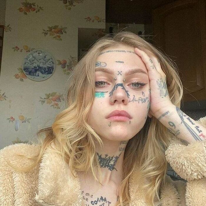 Person with numerous tattoos on face and hand, showcasing unique body art expression.