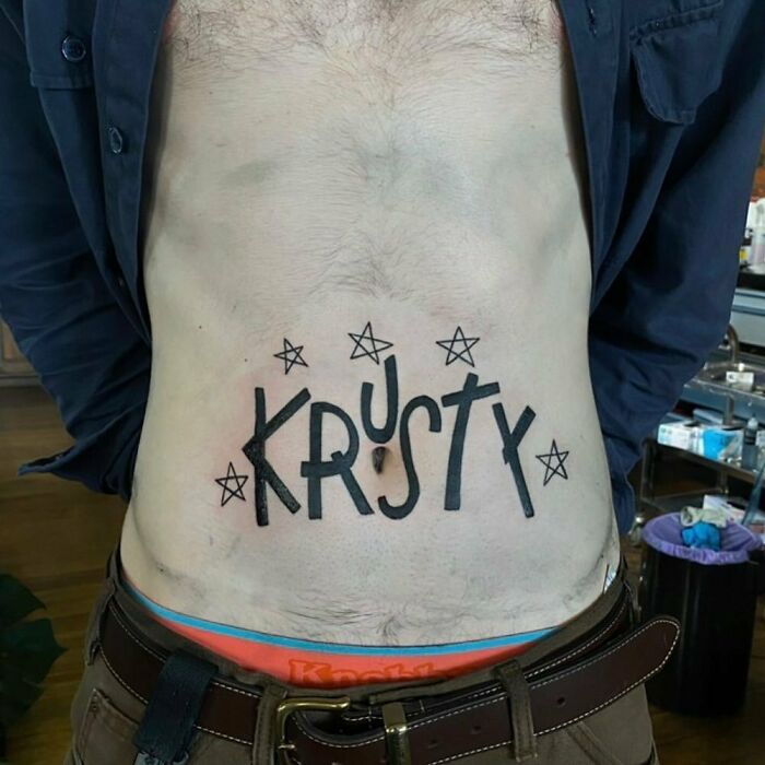 Man with a Simpsons tattoo reading "Krusty" on his stomach, surrounded by stars.