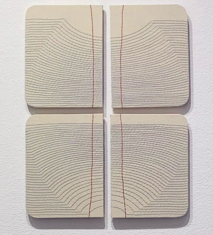 Fabric art resembling notebook pages with embroidery lines and red accents, depicting minimalist book aesthetics.