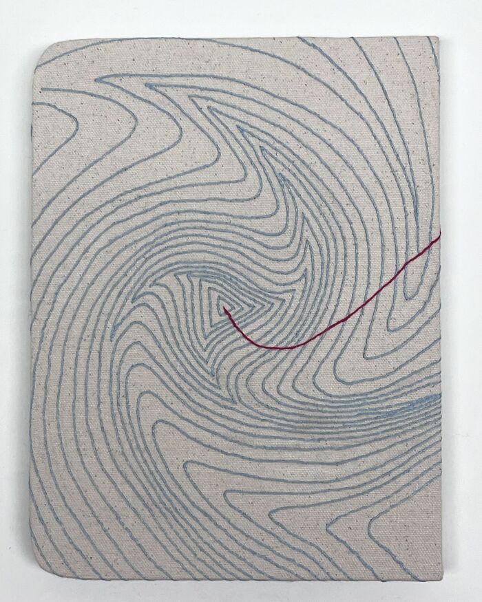 Embroidery art on fabric resembling notebook pages with swirling blue patterns and a red line.