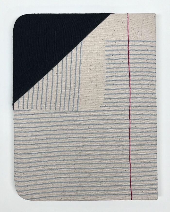Fabric art resembling notebook pages, with blue lines and a red margin, crafted by an artist.