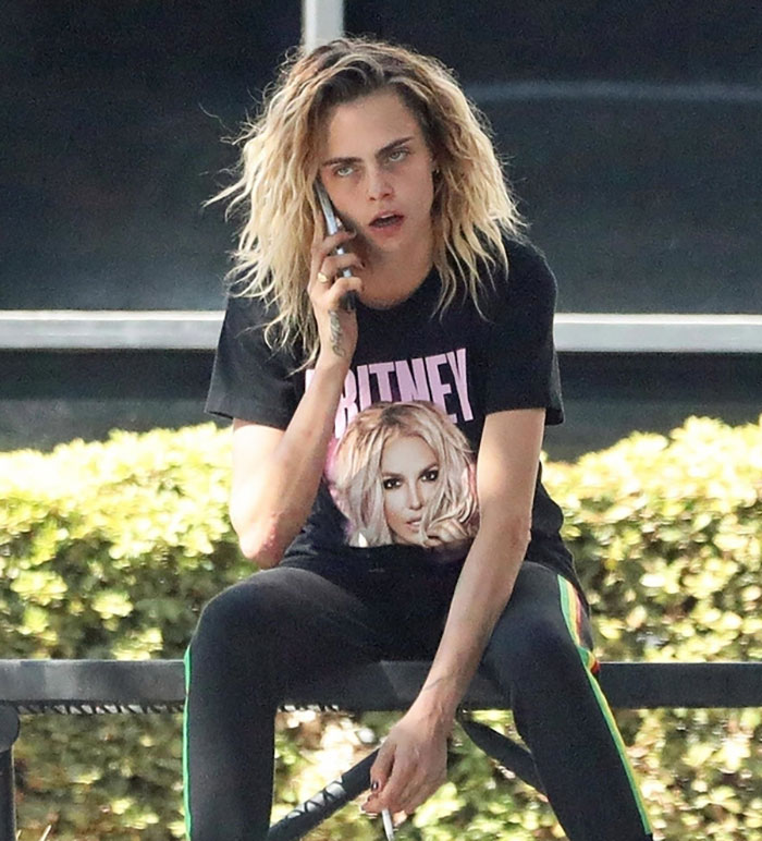 Person with dramatic transformation at Coachella, wearing a black Britney t-shirt, talking on the phone.