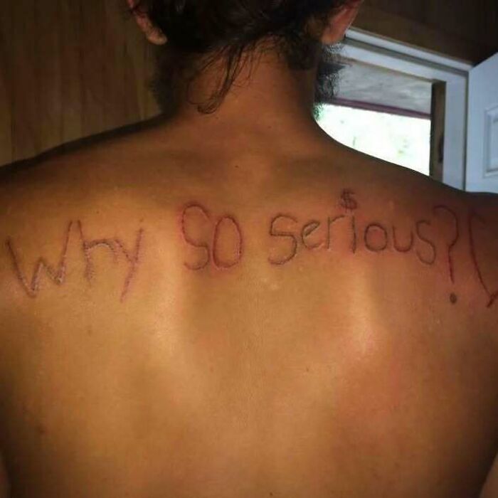 Back tattoo reads "Why so serious?" in red, with uneven letters, illustrating a permanent ink mistake on skin.