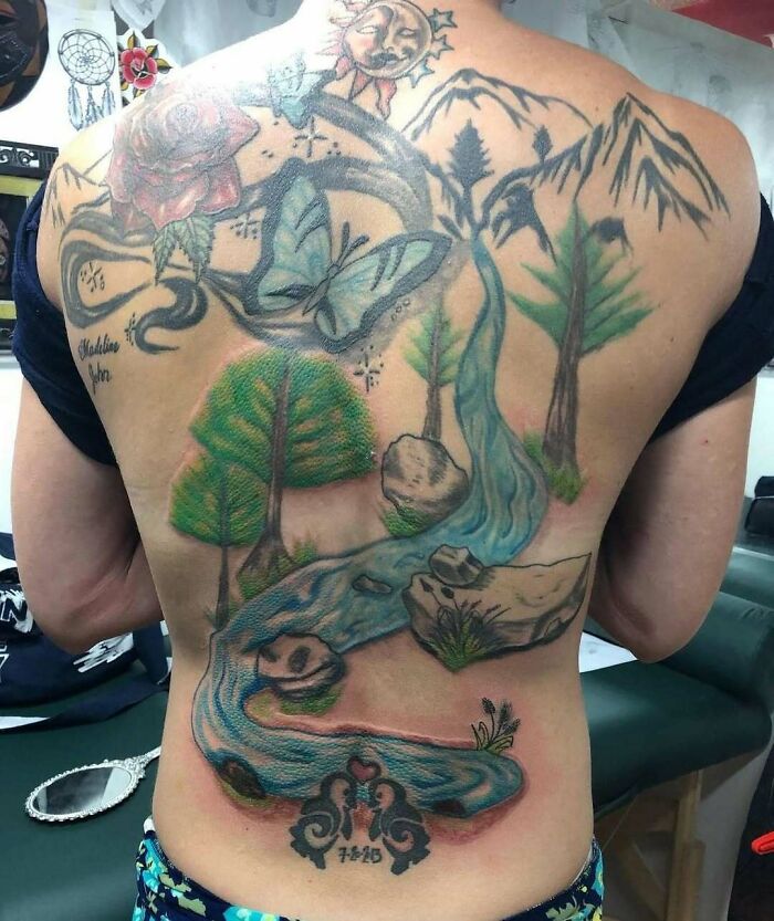 Back tattoo featuring nature elements like a butterfly, trees, and mountains, illustrating permanent mistakes people inked.