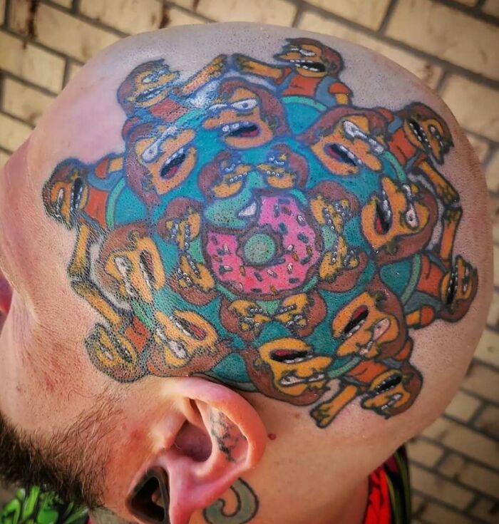 Simpsons tattoo featuring multiple characters encircling a donut on a man's bald head.