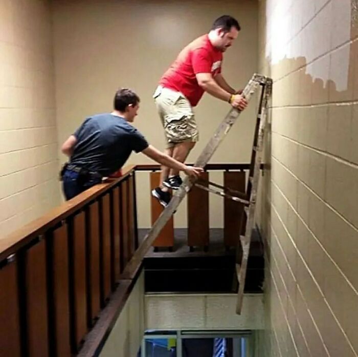 Two men balancing a ladder dangerously over a staircase in a cursed image moment.