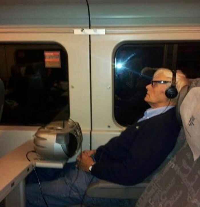Man with headphones sleeping on a train, with a large CRT monitor in front of him, illustrating random cursed images.