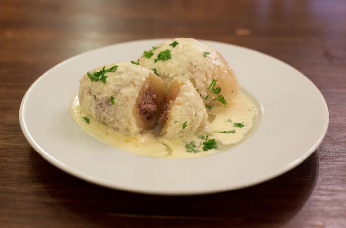 Plate featuring a sliced top dish with creamy sauce and herbs from different countries.
