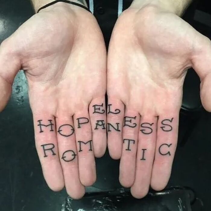 Close-up of hands with a tattoo spelling "hopeless romantic" as a permanent mistake.