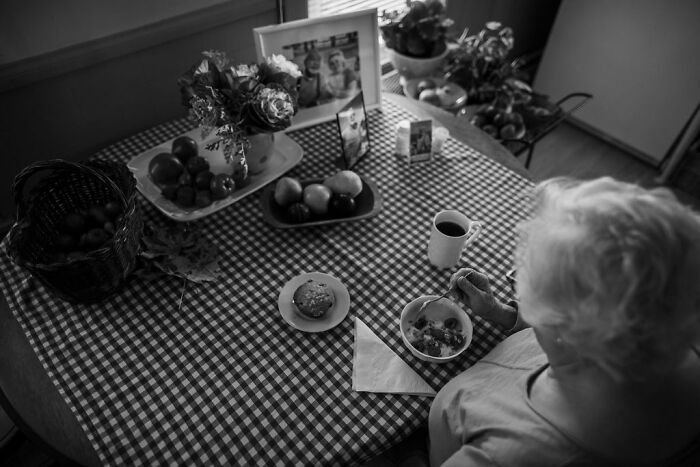 Elderly woman at a checkered table enjoying breakfast, capturing rural life in Maine.