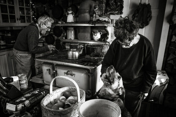 Elderly couple in rustic Maine kitchen with a dog, showing intimate rural life.