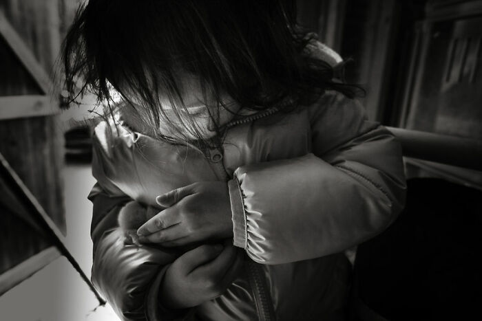Child in a coat gently cradles a small animal, capturing rural Maine's intimate life.