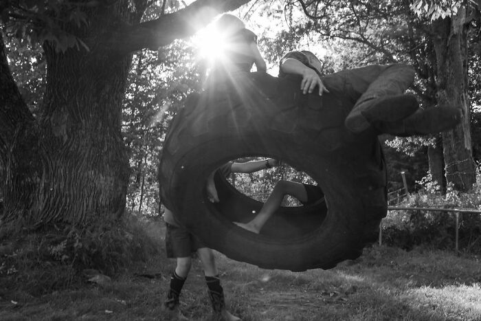 Children playing in a tire swing, capturing rural life in Maine with sunlight filtering through trees.