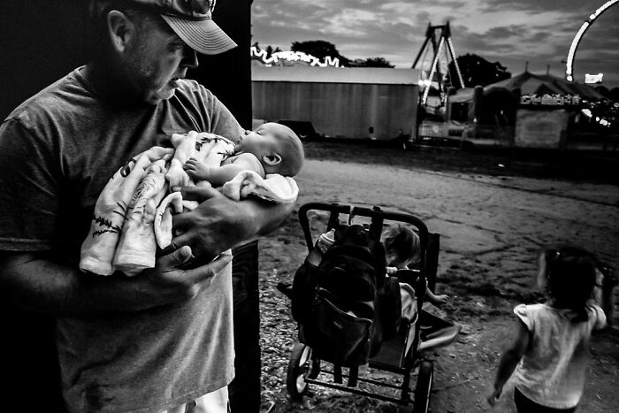 Man holding a baby at a rural fairground in Maine, highlighting intimate rural life.