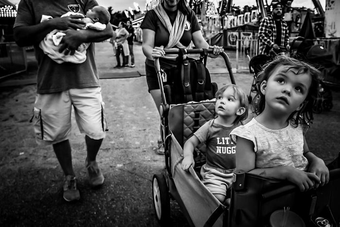 Two young children in a wagon at a rural fair, Maine, with adults nearby in a candid moment.