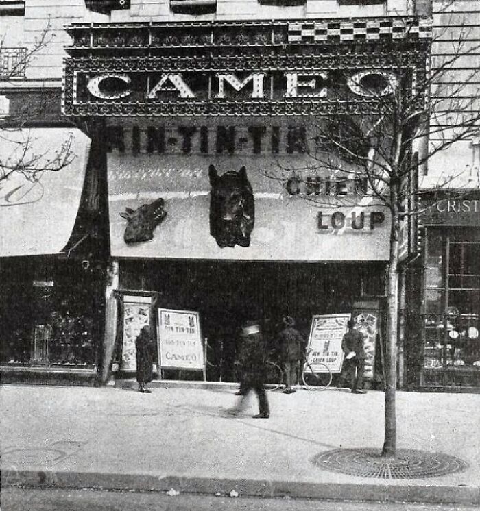 Black and white photo of a European street scene with people walking near a vintage Cameo theater entrance.