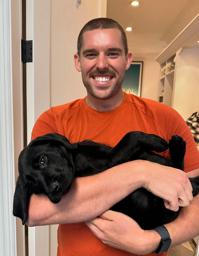 Man in orange shirt holding a black puppy, showcasing impressive weight loss transformation. Man in orange shirt holding a black puppy, showcasing impressive weight loss transformation.