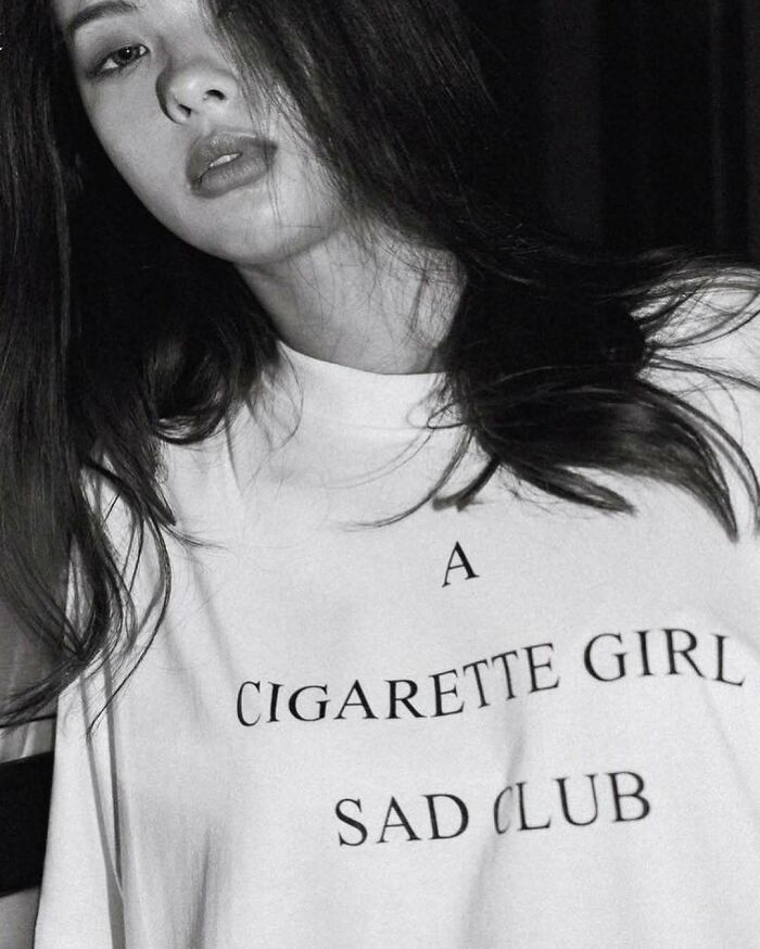 Woman in a T-shirt with "A Cigarette Girl Sad Club" printed, humor in translation.