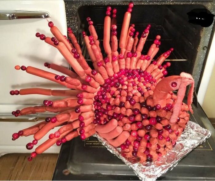 Unappetizing food sculpture resembling a turkey made from hot dogs and cherries on a foil-covered tray.