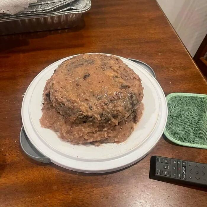 Unappetizing food dish resembling a mushy cake on a plate, with a remote nearby on a wooden table.
