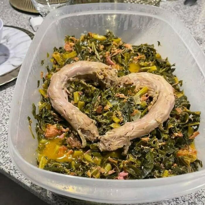 Unappetizing food in a container with meat forming a heart shape on top of cooked greens.