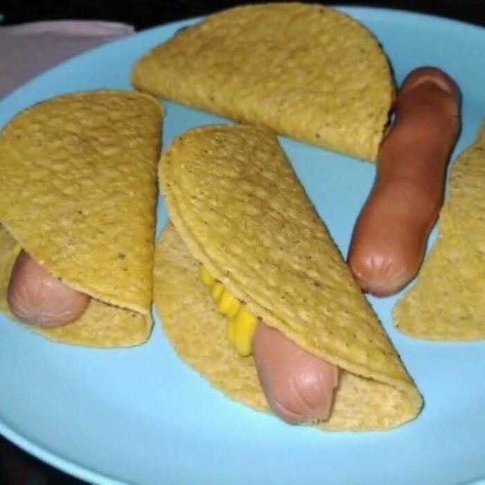 Unappetizing tacos with hot dogs and corn on a blue plate.