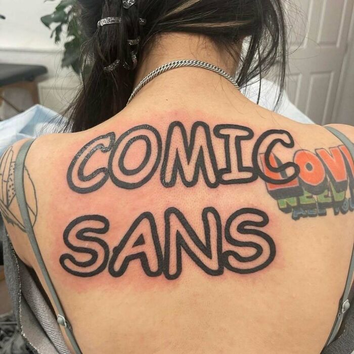 Tattoo of the words "Comic Sans" in bold, black letters on a person's upper back.