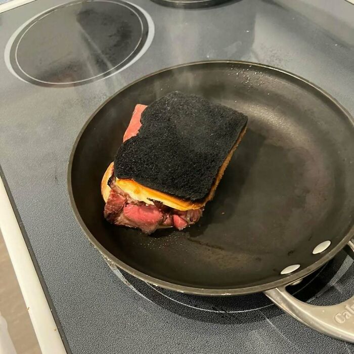 Burnt sandwich with charred bread in a frying pan, showcasing unappetizing cooking for bae.