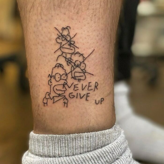 Simpsons tattoo of a character with "Never Give Up" text on a leg.