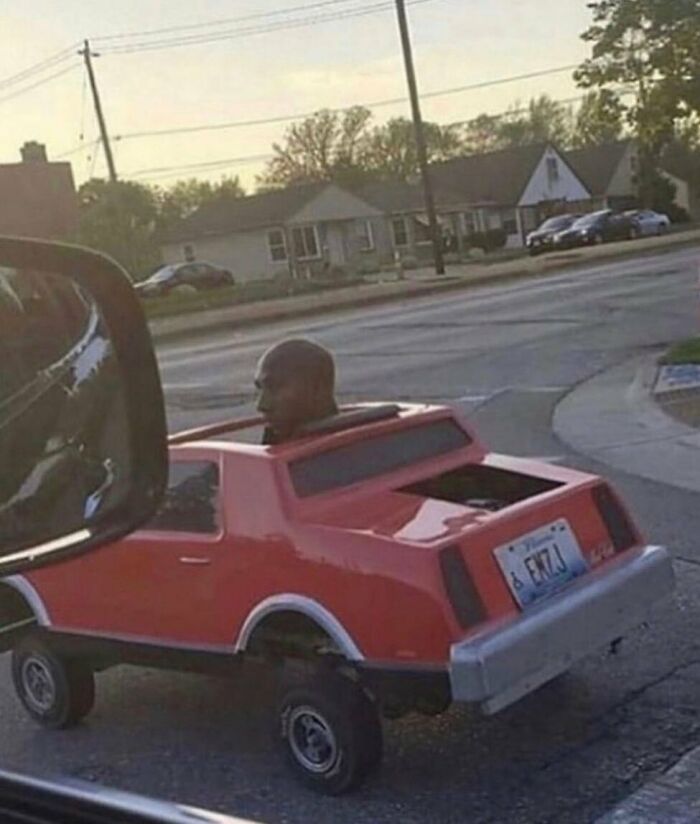 A man driving a small, red car with a humorous look, illustrating a random cursed image scenario.