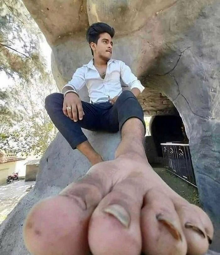 Man sitting with exaggerated large foot in foreground, creating a humorous and random cursed image illusion.