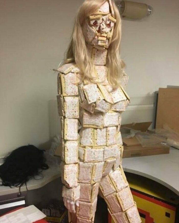 A mannequin covered in pop-tarts and wearing a blonde wig, showcasing a bizarre cursed image in an office setting.